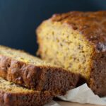 Banana Bread Recipe – Golden banana bread loaf sliced on a wooden cutting board.