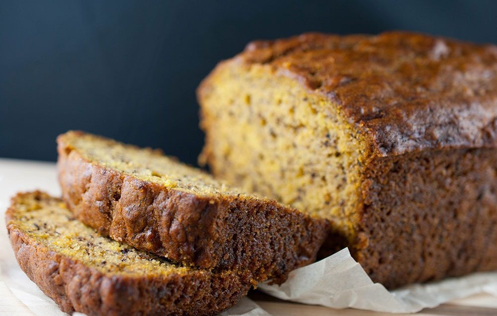 Banana Bread Recipe – Golden banana bread loaf sliced on a wooden cutting board.